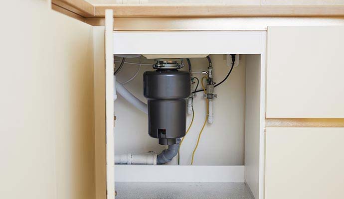 A black garbage disposal unit installed under a kitchen sink