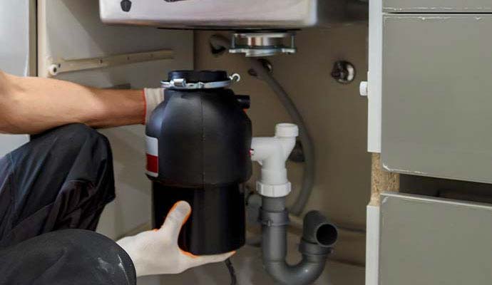 A technician of M&J Restoration installing a garbage disposal unit after restoration