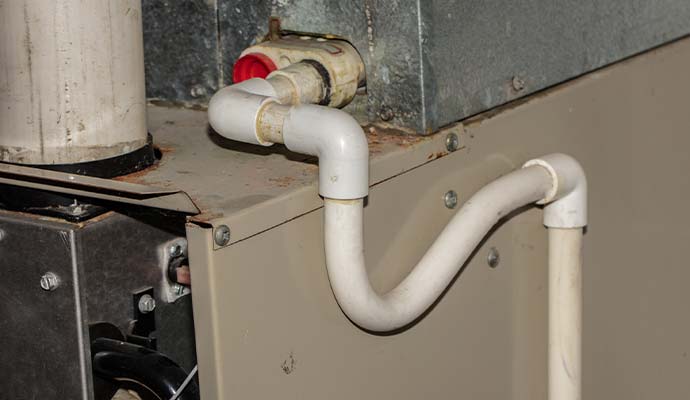 A white PVC P-trap condensate drain pipe connected to an indoor HVAC system