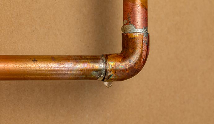 Close-up of a leaking copper pipe elbow joint with a water droplet