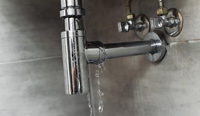 Water dripping from a leaking chrome sink trap under a bathroom sink