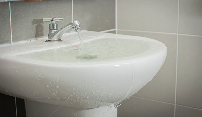 Clogged bathroom sink overflowing with water onto the floor causing potential household water damage