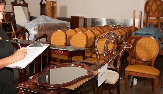 Professional restoration specialist documenting and inventorying antique furniture and household contents in a climate-controlled facility