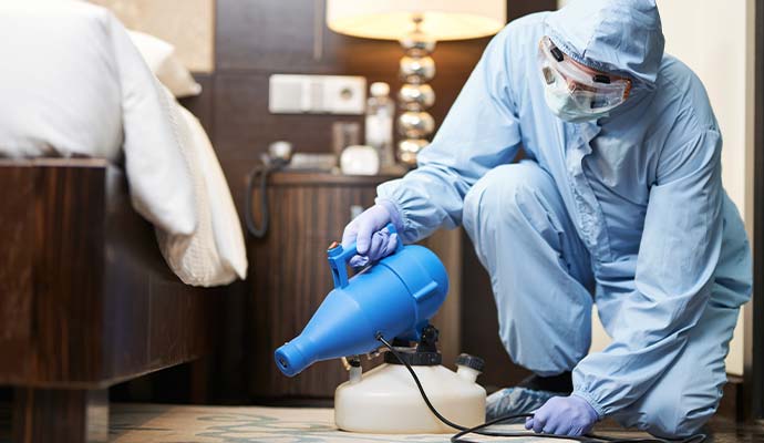 Technician in protective suit fogging smoke deodorizer in bedroom