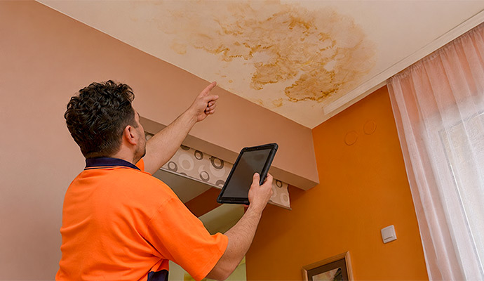 Restoration technician inspecting ceiling water damage with digital tablet