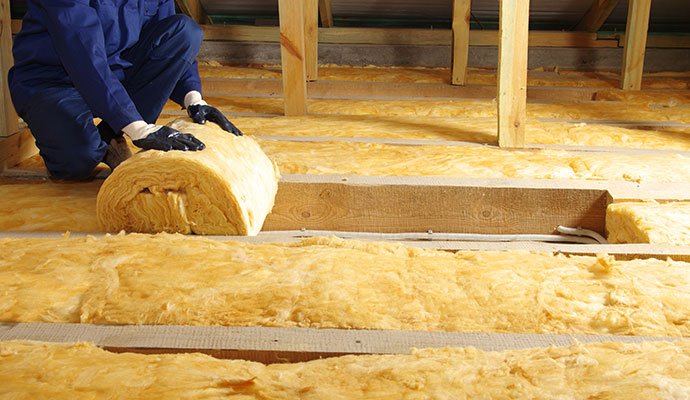Worker installing fiberglass insulation in attic